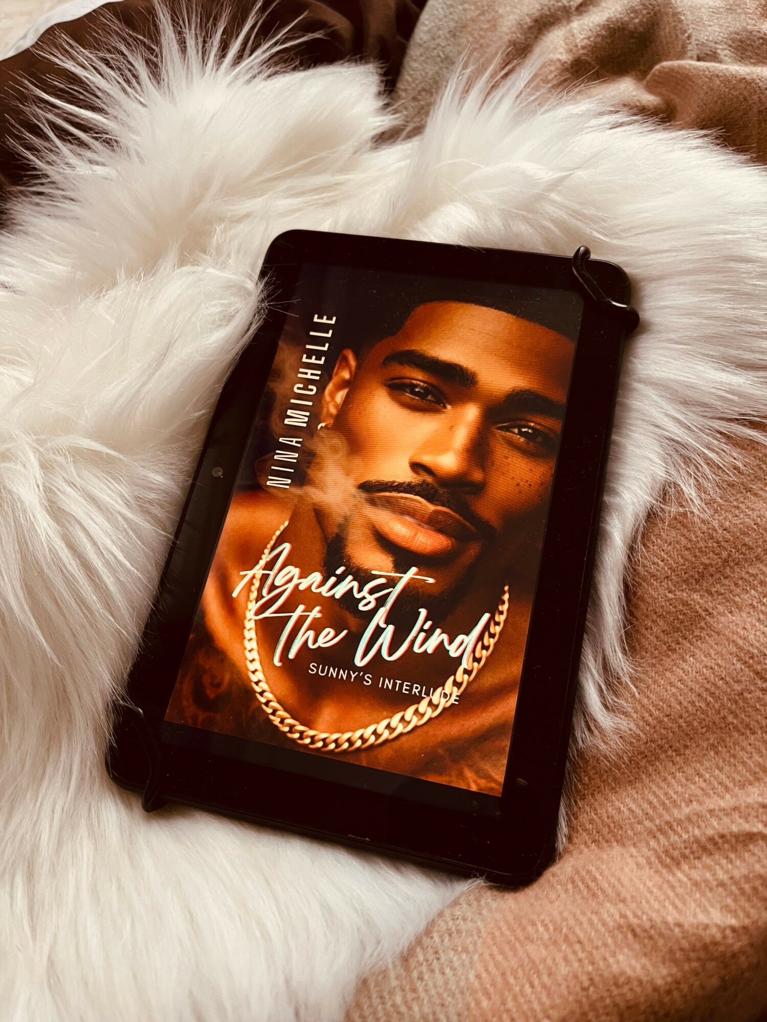 A tablet displaying a portrait of a man with a chain necklace, resting on a fluffy white surface.