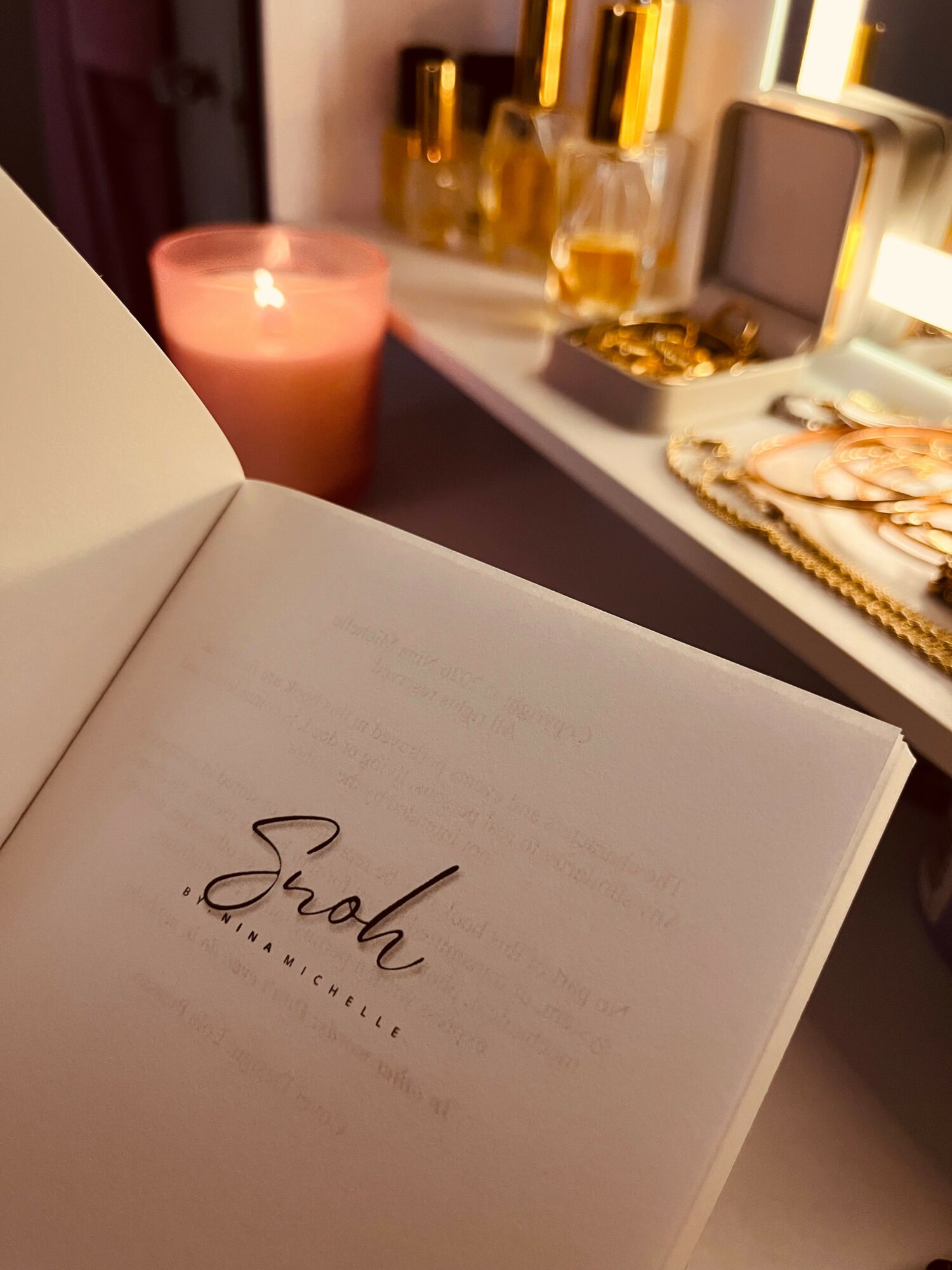 Open book with the word 'Snoh' on the page, background includes candles and decorative items on a shelf.