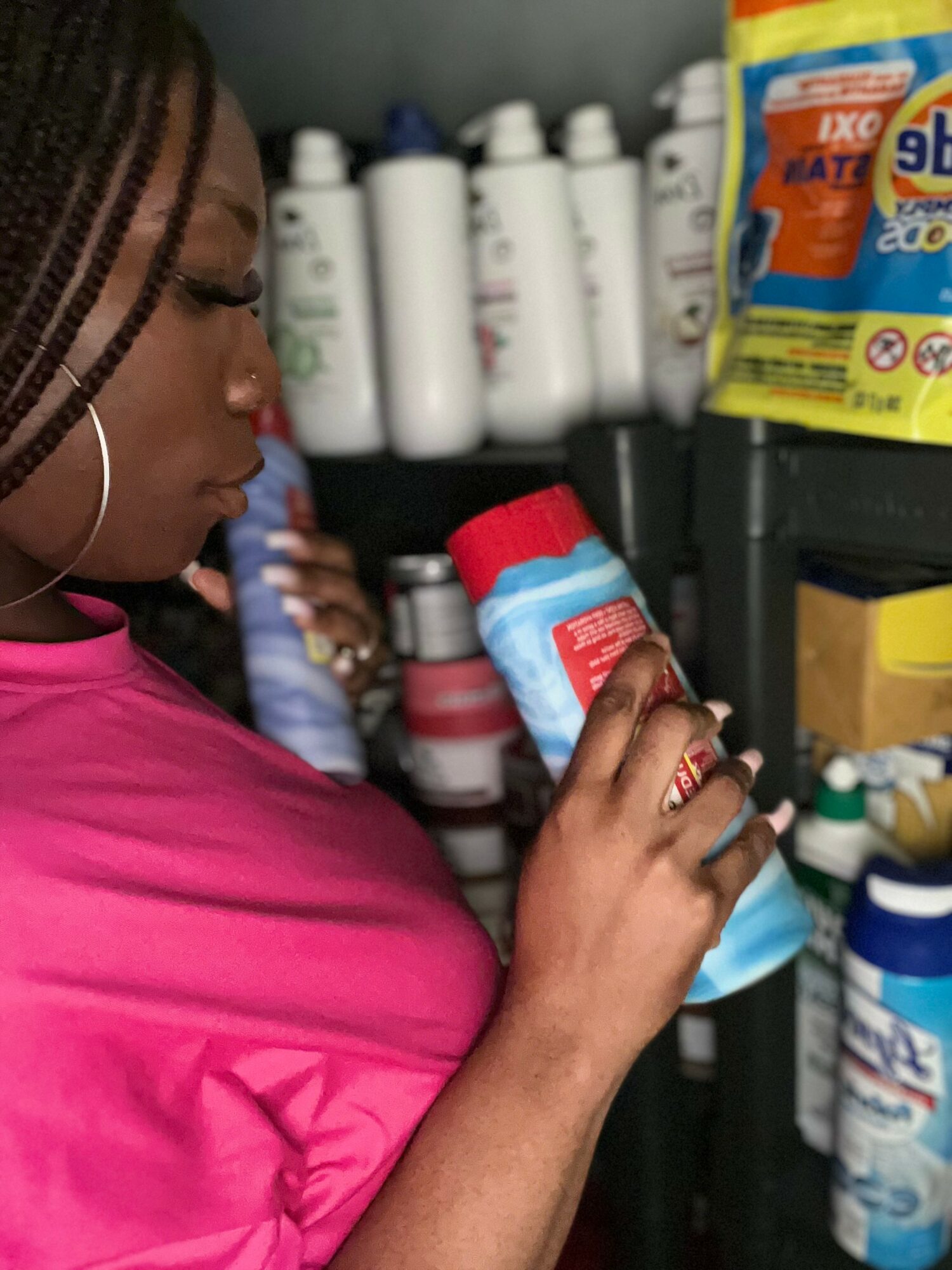 Person in pink shirt holding a spray bottle in a store aisle with cleaning products on shelves.