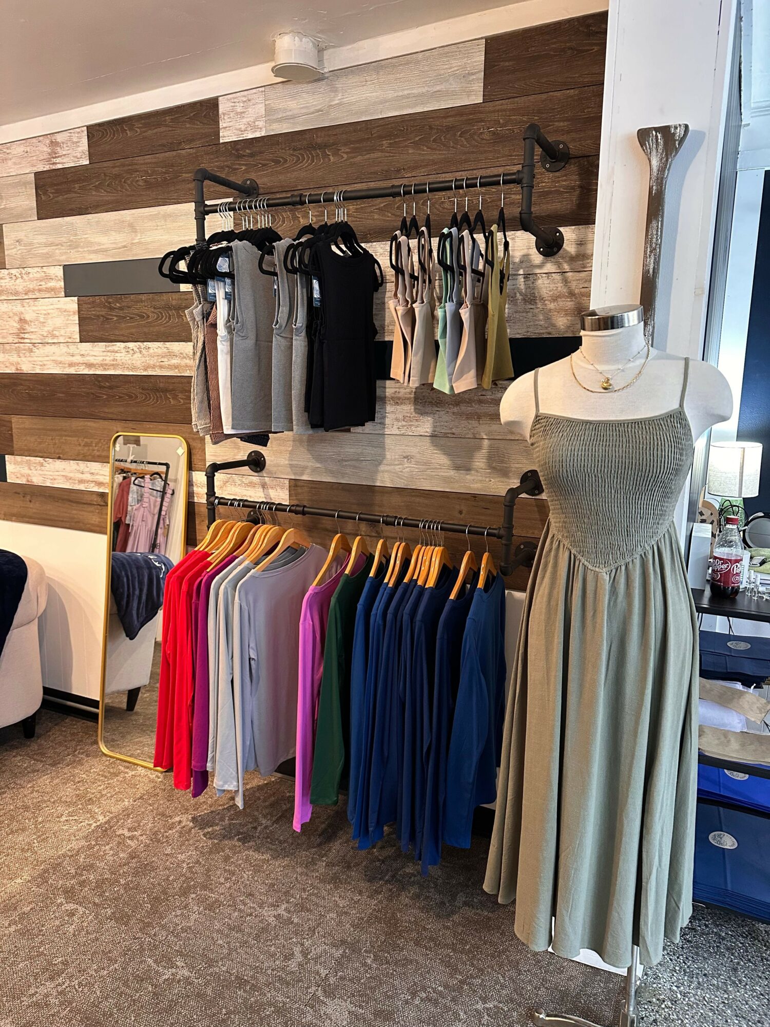 Display of folded clothes, a lamp, and a mirror in a retail store, with clothing racks and shelves in the background.