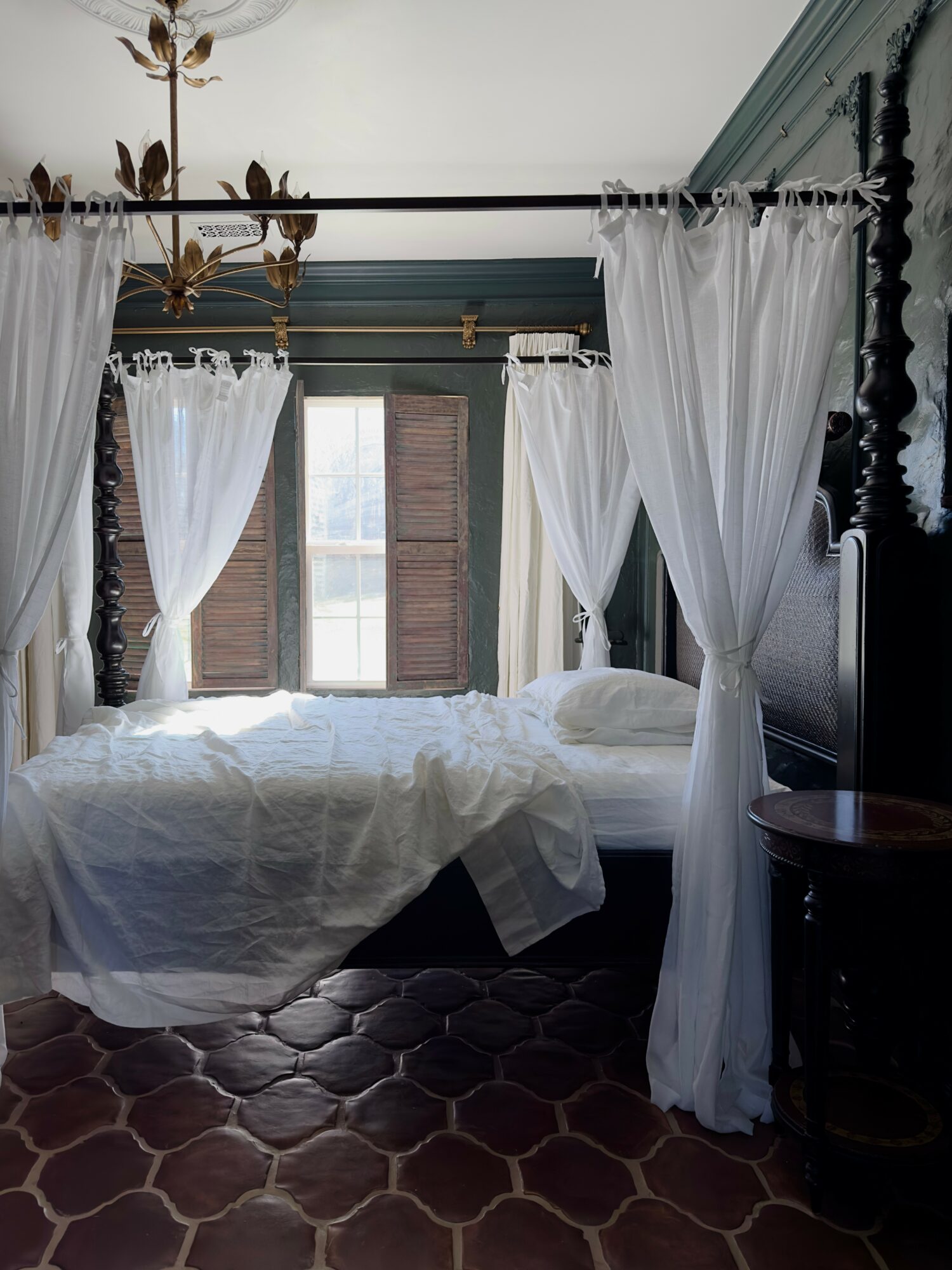 Bedroom with four-poster bed, white curtains, and a window with shutters, decorated in vintage style.