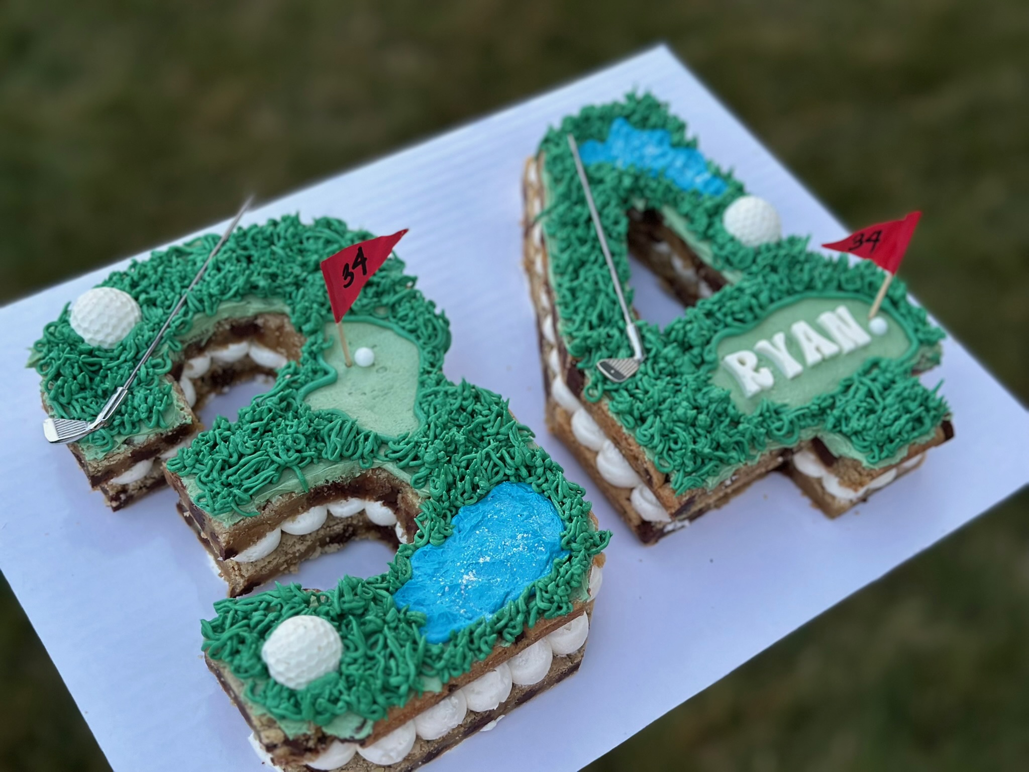 Two birthday cake cookies decorated with green and blue icing, white pearls, and red flags, spelling 'RYAN'.