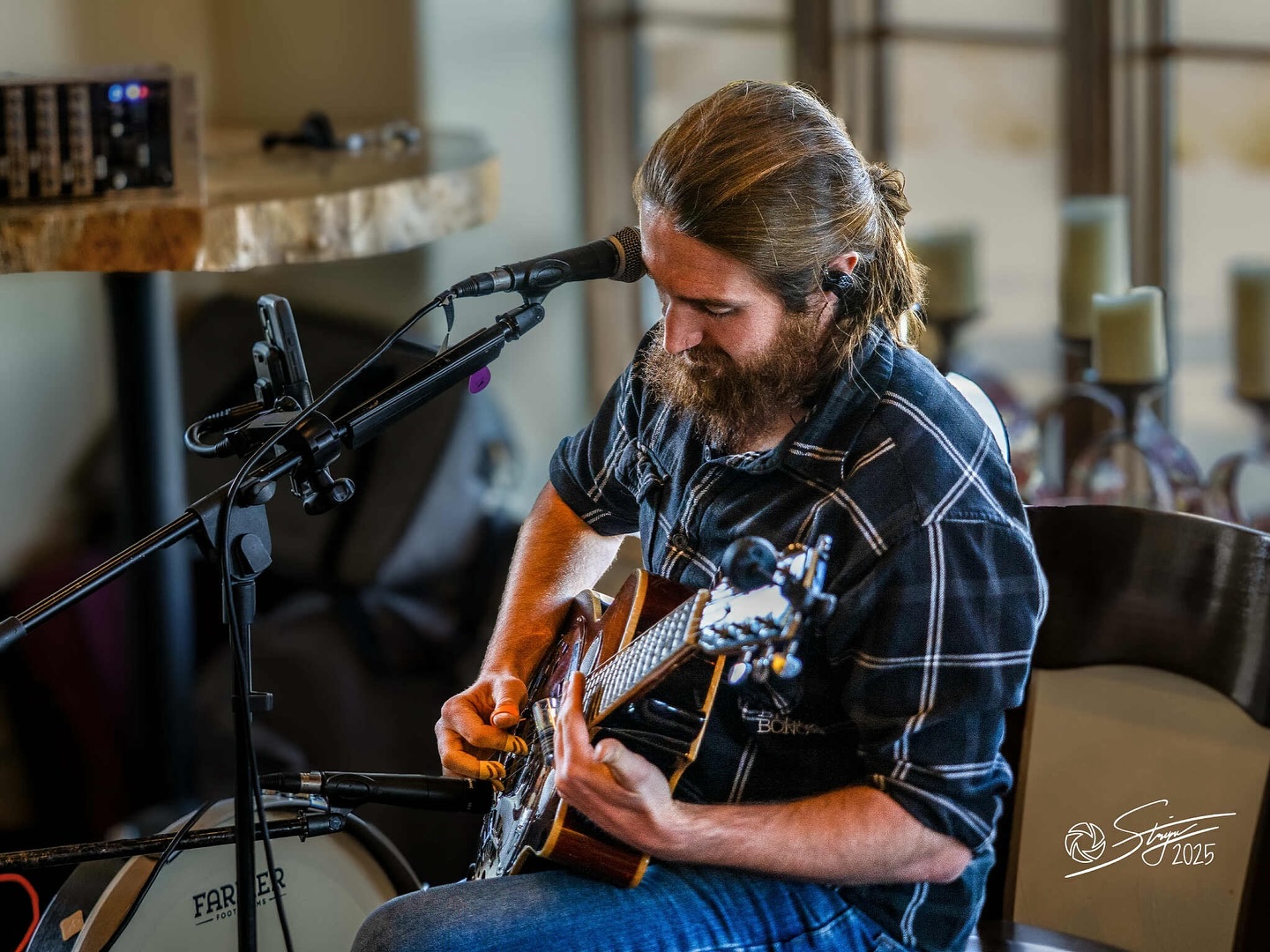 Man with long hair and beard playing an acoustic guitar in a room with candles and music equipment
