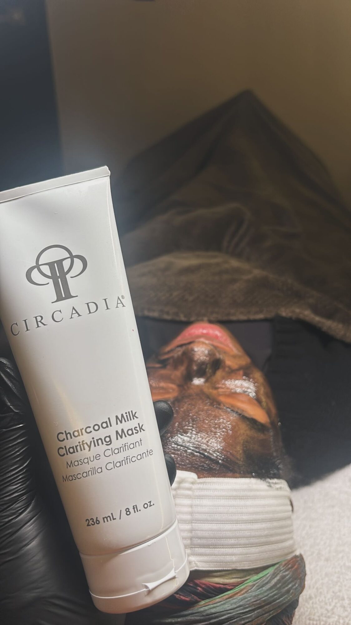 Person lying down with a face mask, eyes closed, and a towel on their forehead, in a relaxing setting.