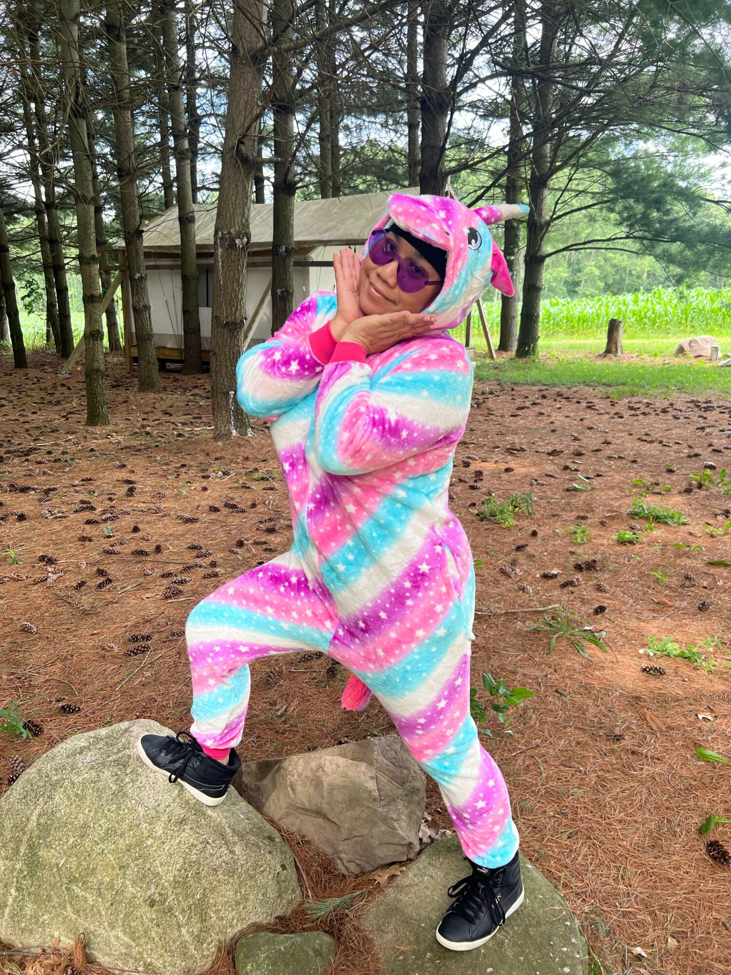 Child in colorful onesie and hat taking a selfie outdoors in a wooded area.