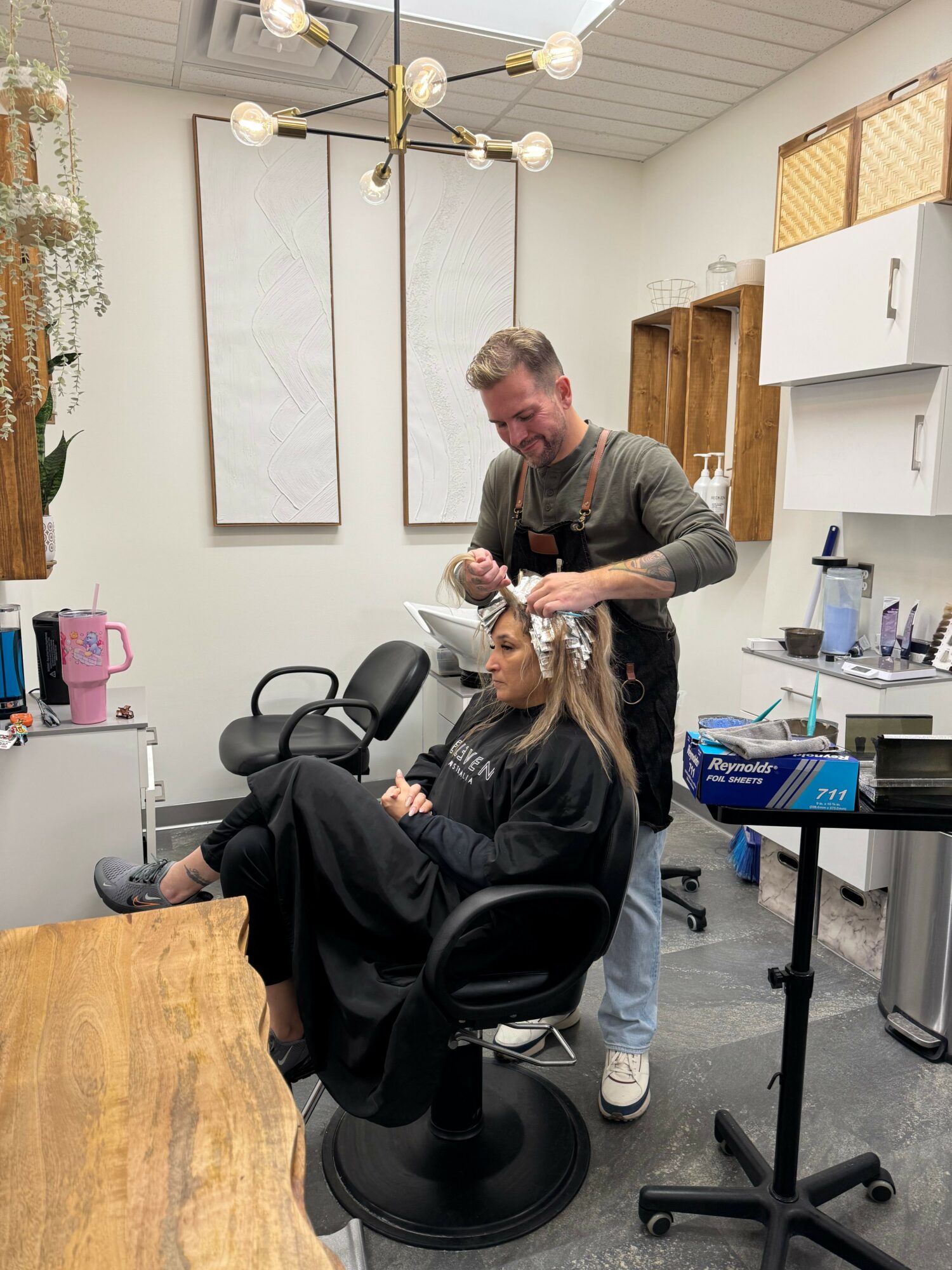 Person receiving makeup or hair styling in a salon or studio, with a stylist working on their hair or face, seated in a chair.