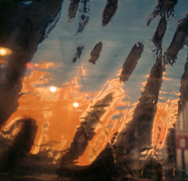 Reflected palm trees and sky in water with sunset colors, distorted by ripples.
