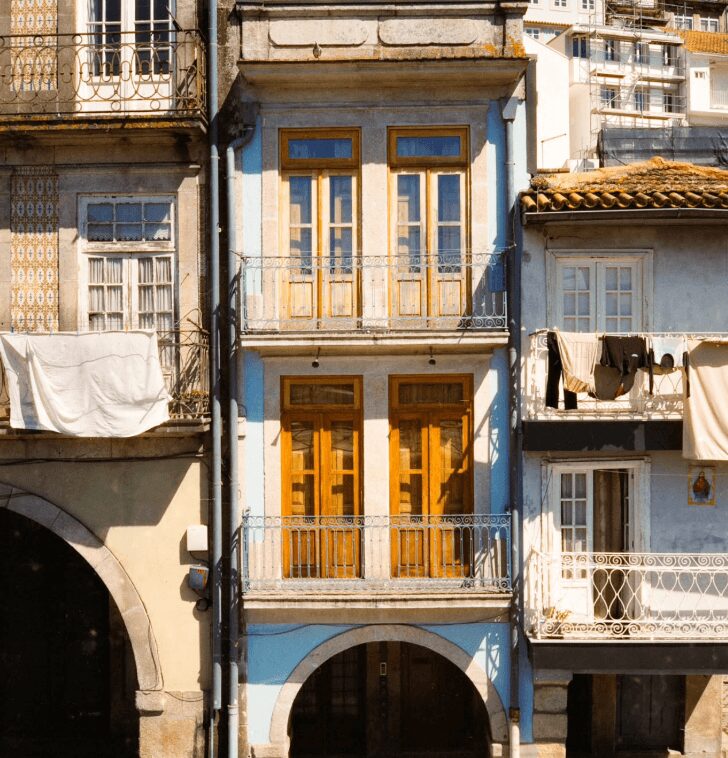 Three-story building with yellow doors and windows, balconies, and neighboring buildings with laundry hanging outside.
