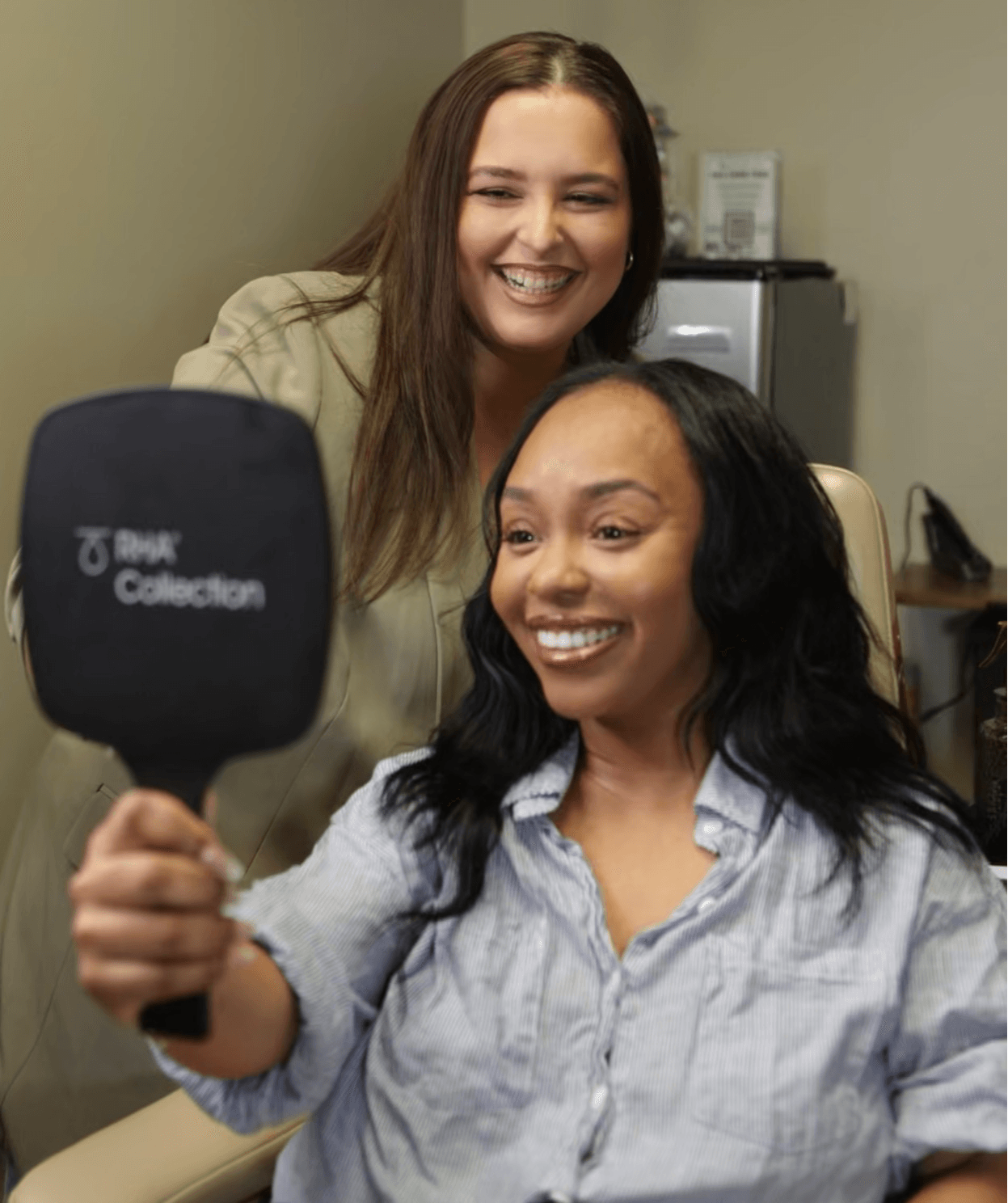 Two women smiling, one holding a microphone, in an indoor setting.