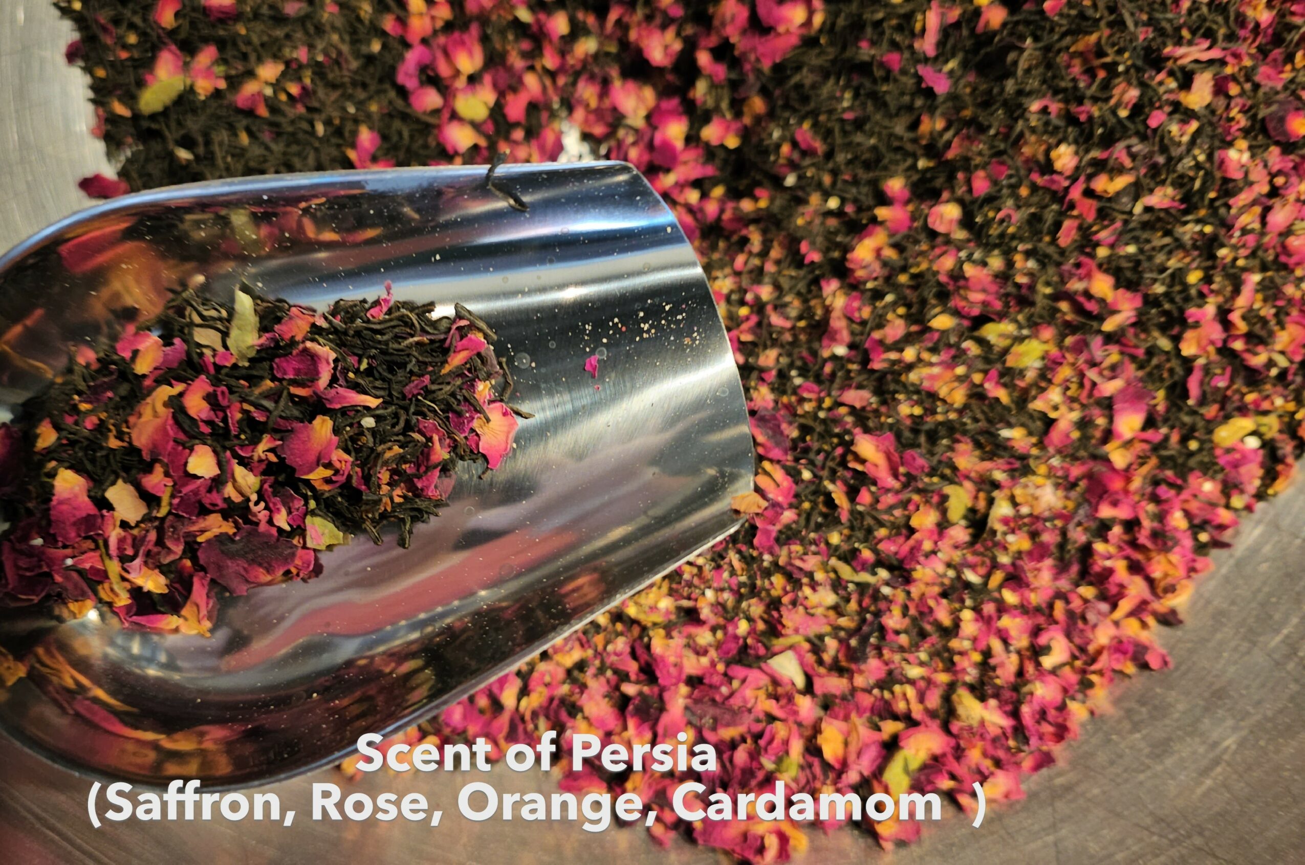 A metal scoop filled with pink, orange, and yellow flower petals, with more petals scattered on the ground nearby.