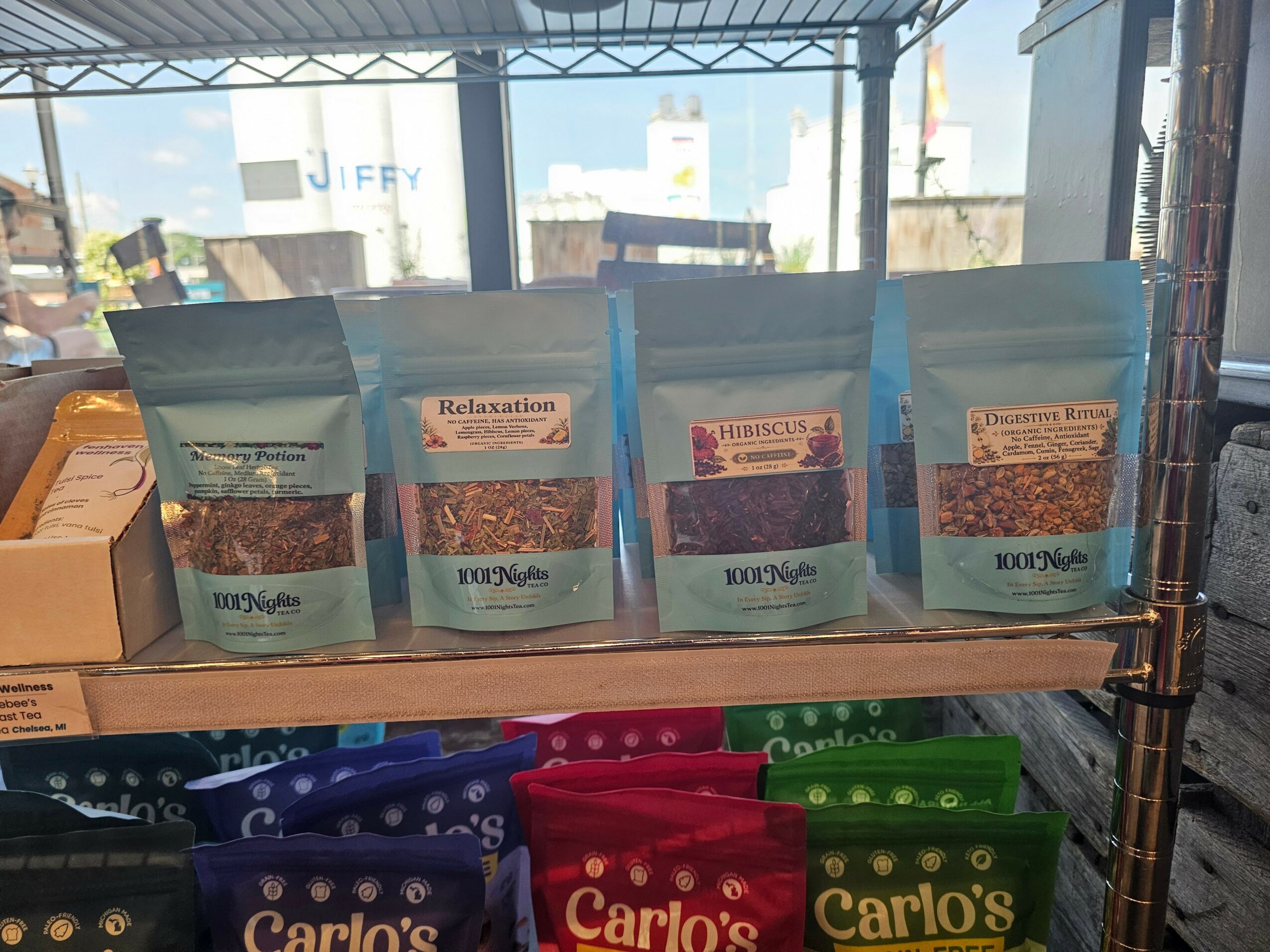 Four blue packages on a shelf with a window in the background, sunlight coming through, and a cityscape outside.