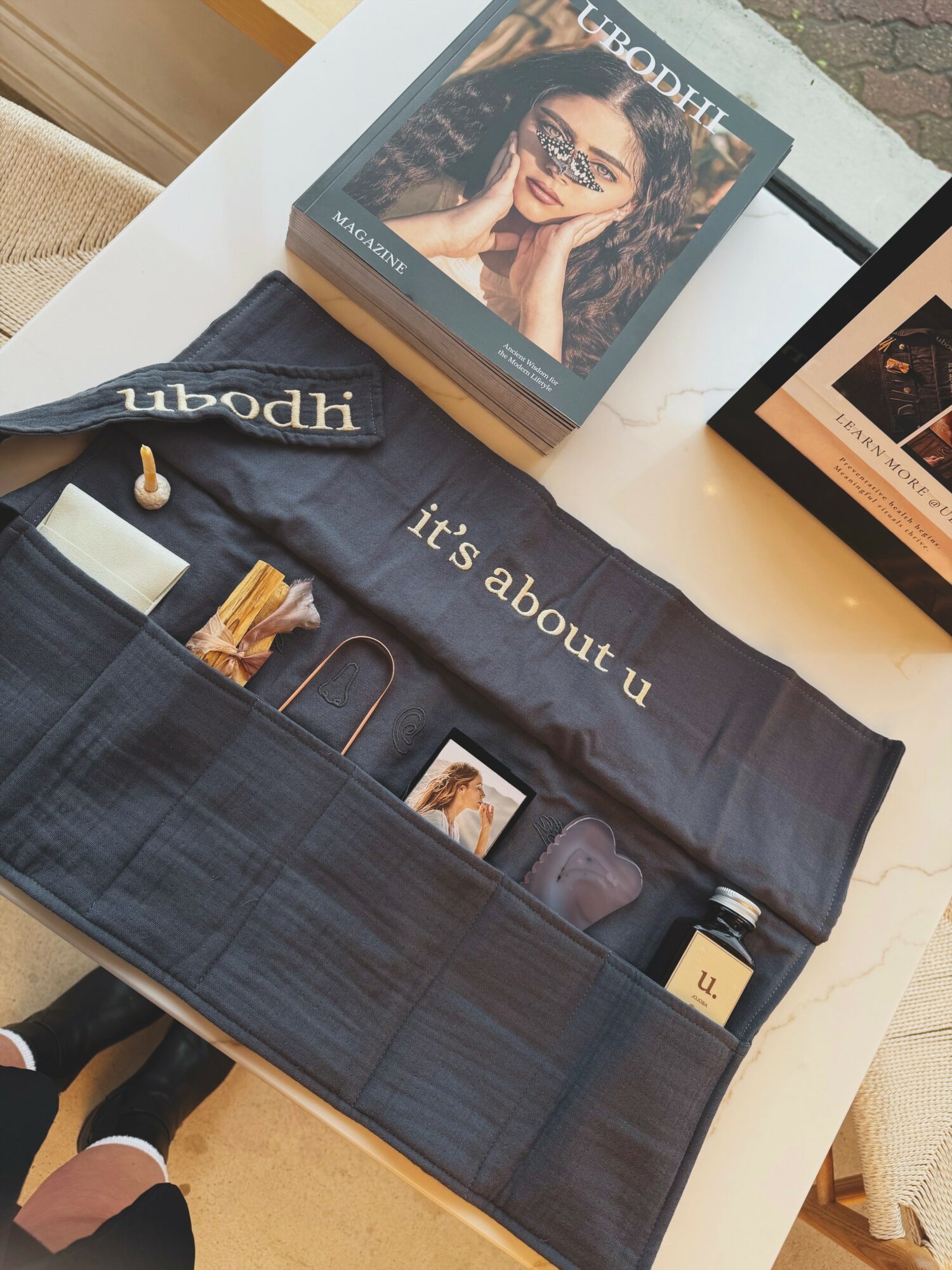 Open black fabric case with various items inside, on a white table with books and a laptop nearby.
