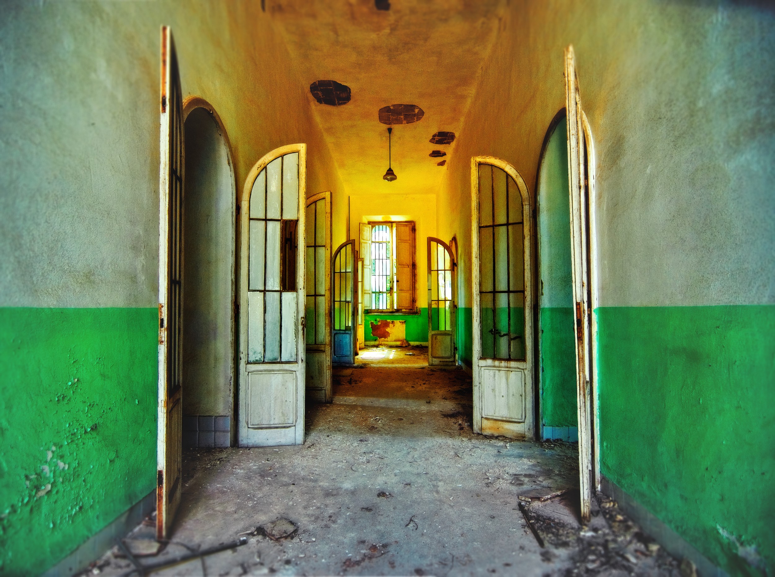 Long corridor with open doors, green lower walls, yellow upper walls, and a window at the end.