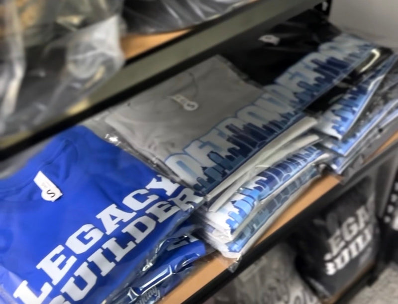 Stack of folded blue and gray clothing with text, on a shelf in a store.