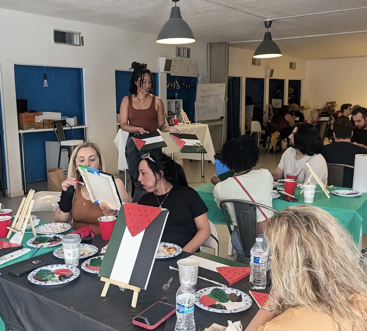 Group of people at a table with watermelon-themed decorations, eating and talking in a decorated room.