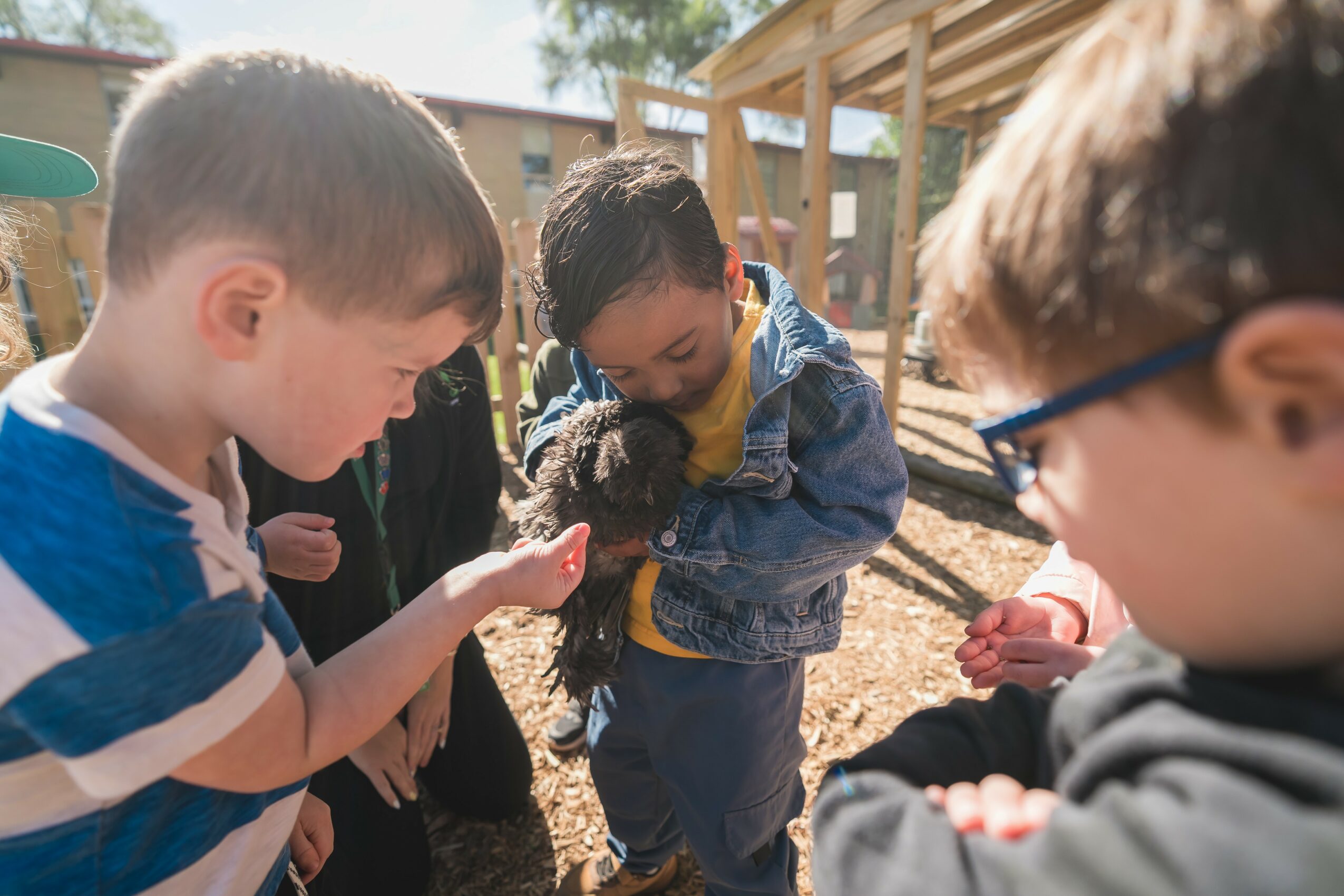 Children outdoors, smiling and interacting, with playground equipment and trees in the background.