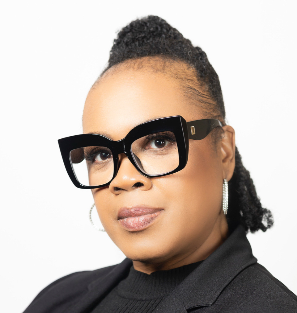 Woman with glasses and earrings, wearing a black blazer, looking at the camera against a white background.