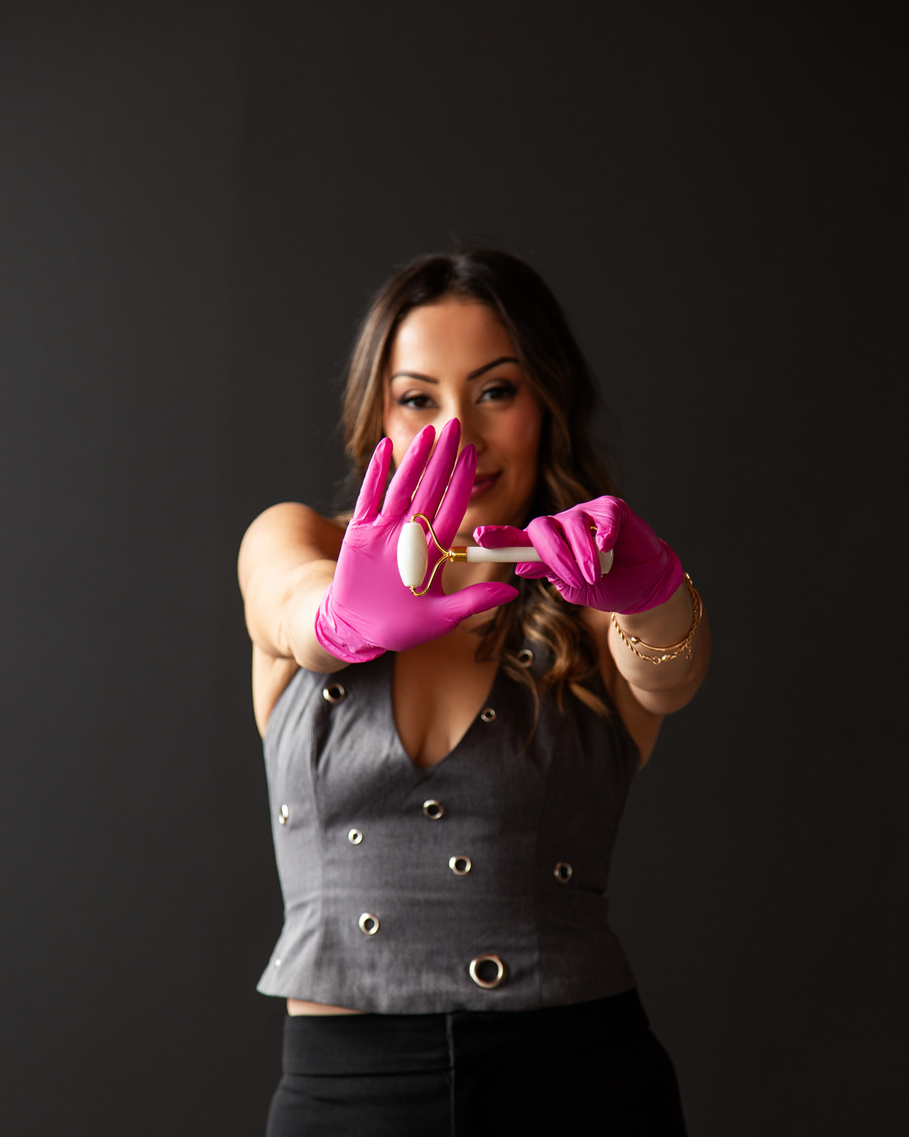 Woman with long hair wearing pink gloves, holding a ring, and smiling, against a dark background.