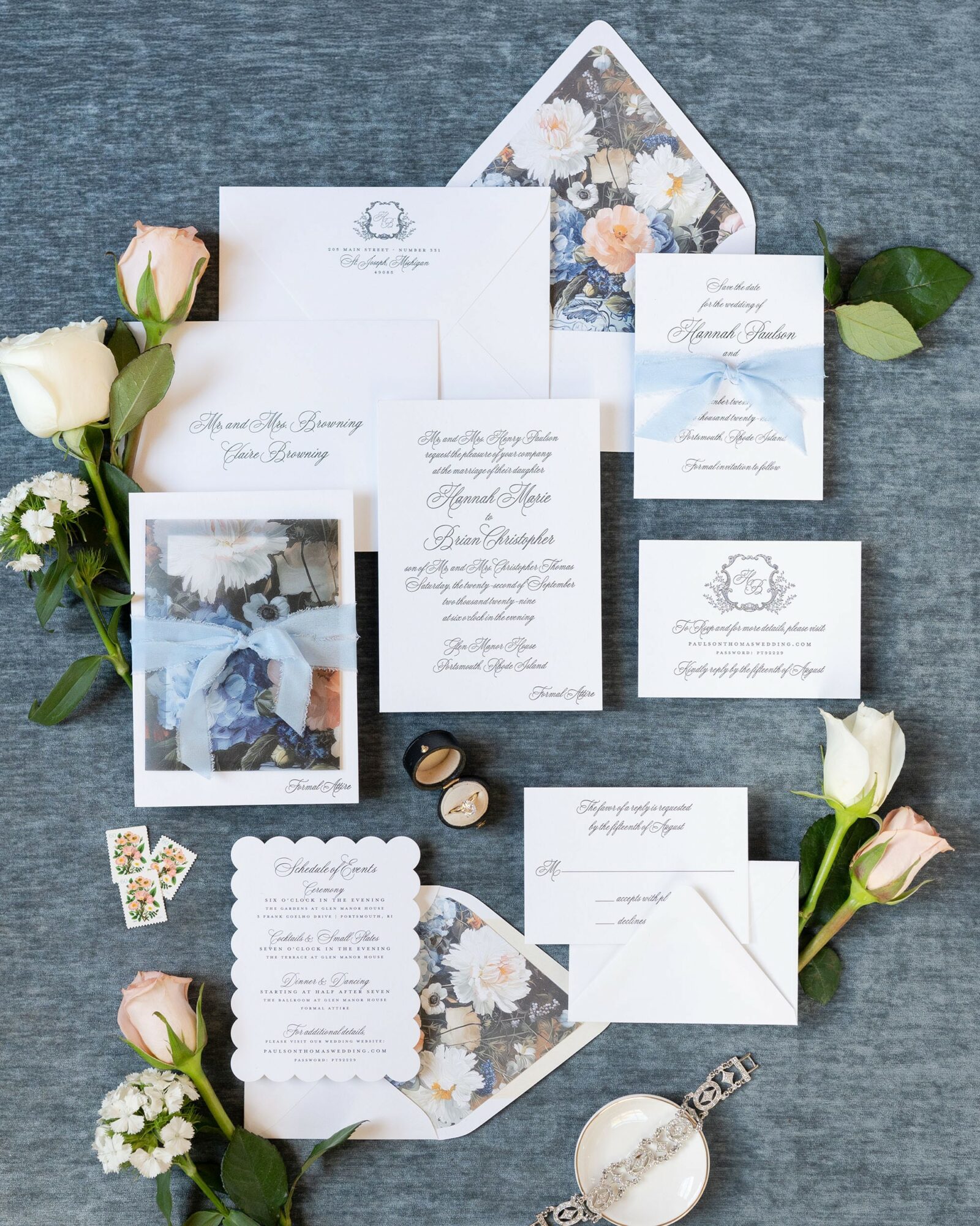 Wedding invitation suite with floral accents, photos, rings, and decorative elements on a blue surface.