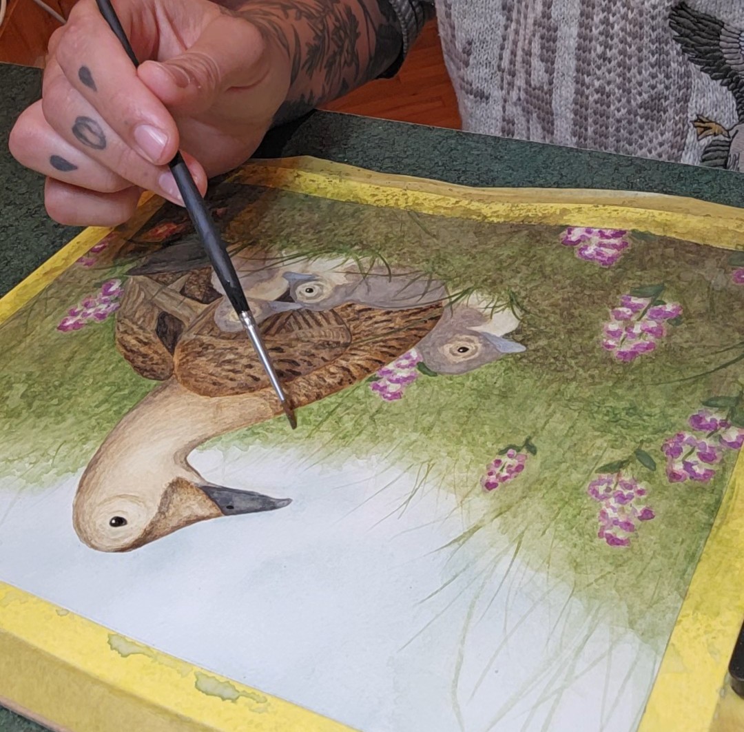 Person painting a detailed bird with a paintbrush on a nature scene, surrounded by pink flowers.