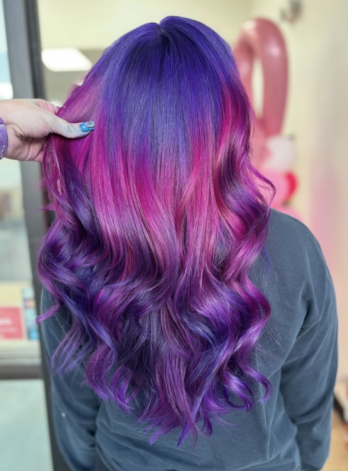 Back view of a person with long, wavy hair dyed in purple and pink shades.
