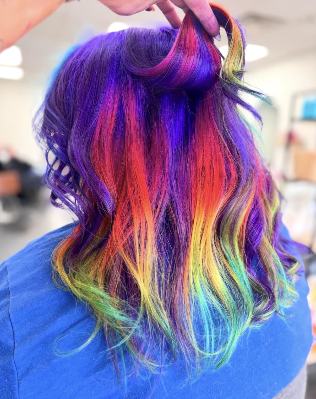 Person with long, wavy hair dyed in rainbow colors, including purple, pink, orange, yellow, green, and blue.