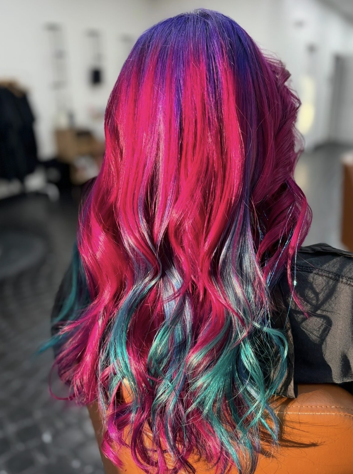 Back view of a person with long, wavy hair dyed in pink, purple, and teal colors.