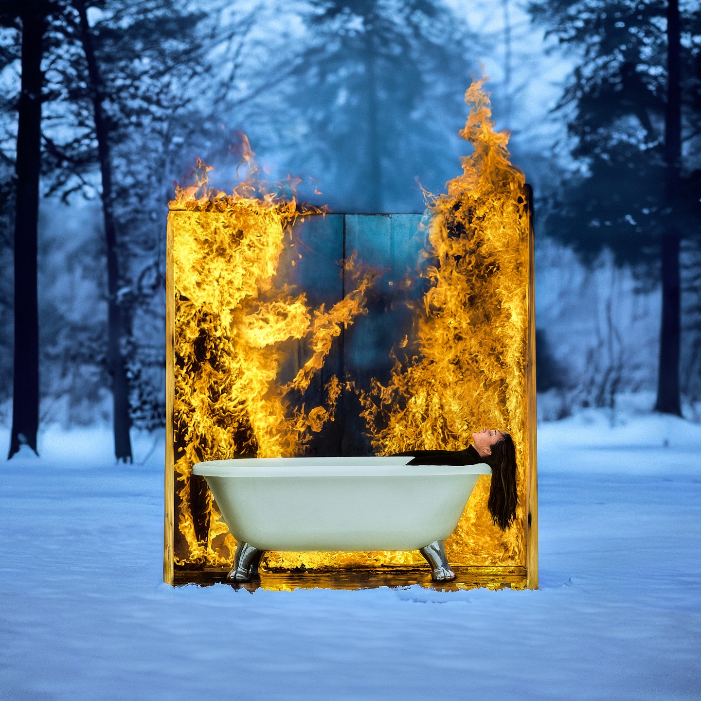 A bathtub with fire behind a glass panel in a snowy forest, with trees and snow in the background.