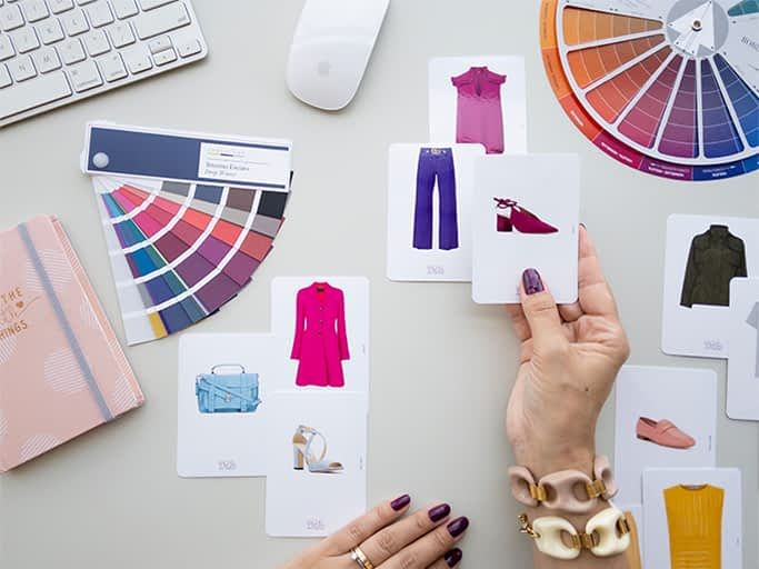Hand holding a card with a purple dress, color palette, color wheel, and various fashion items on a white background.