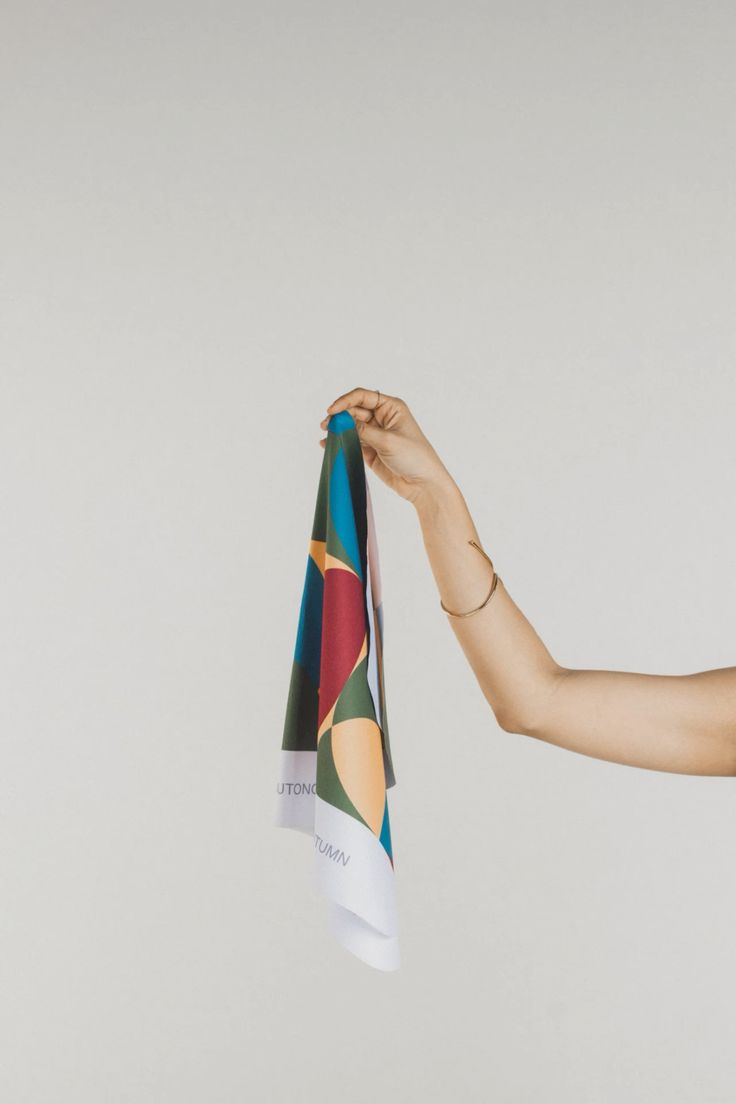 Person's arm holding a colorful scarf or cloth against a plain background.