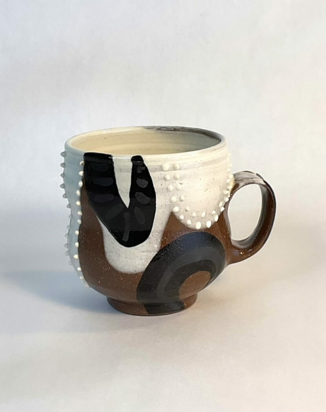 Ceramic mug with a black, white, and brown abstract design, placed on a white surface with a plain background.