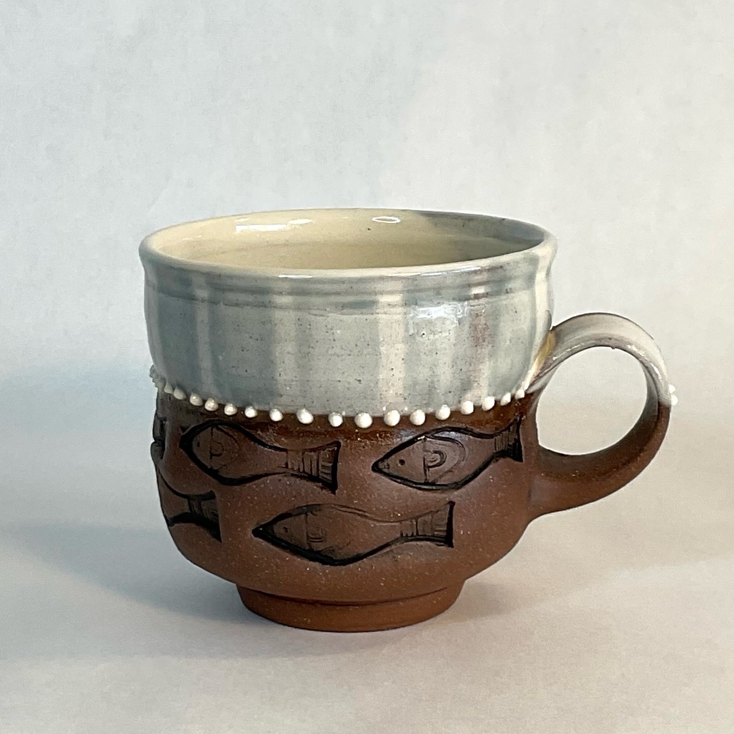A ceramic cup with a fish pattern, two-tone glaze, and a handle, placed on a plain surface.