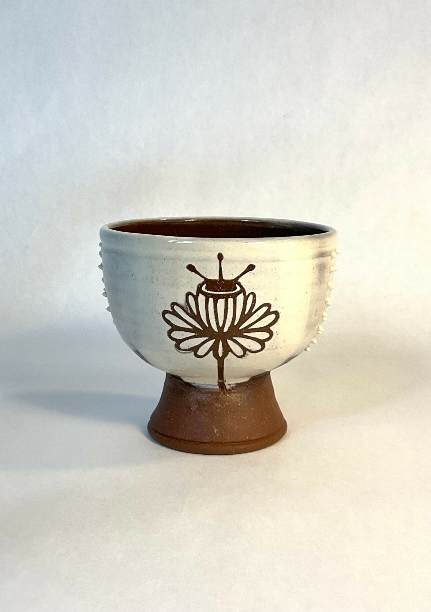 Ceramic cup with a floral design and a ladybug illustration, on a white surface with a plain background.