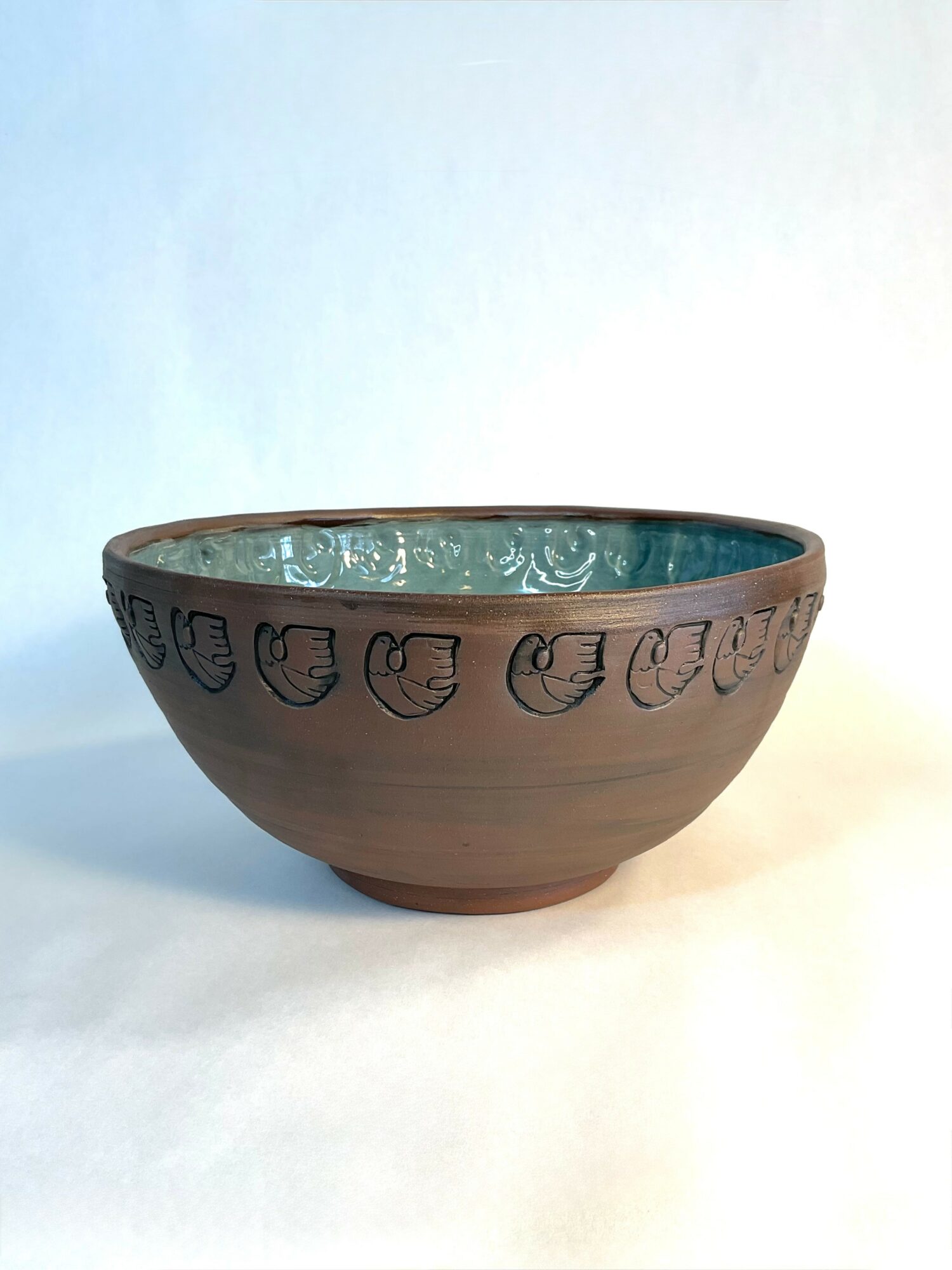 Clay bowl with decorative face patterns around the rim, interior appears glazed with a textured surface, on a plain background.