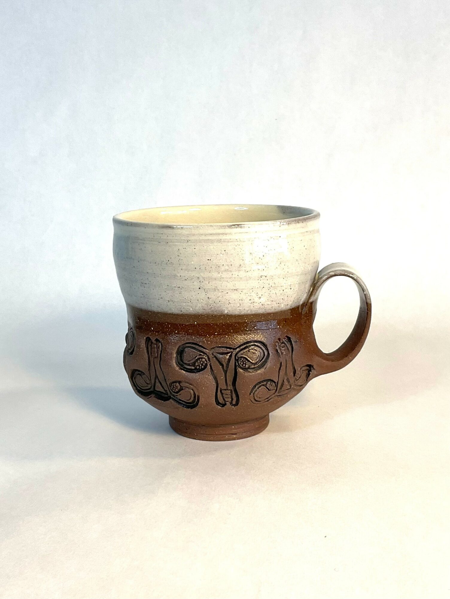 A ceramic mug with a two-tone design, featuring a cream upper part and a brown lower part with decorative patterns, on a white surface.
