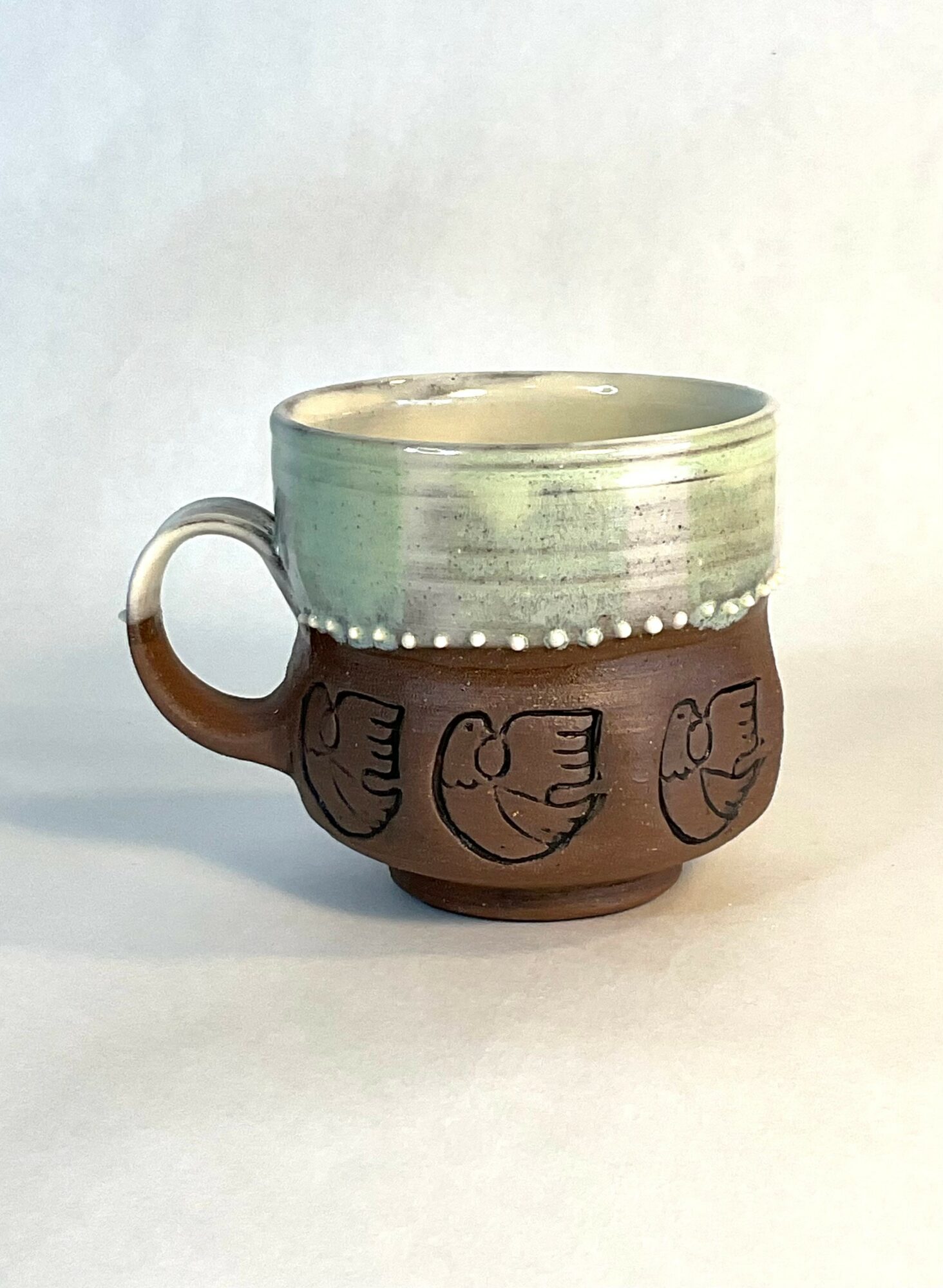 Ceramic mug with fish designs, glazed in green and brown, on a plain background.