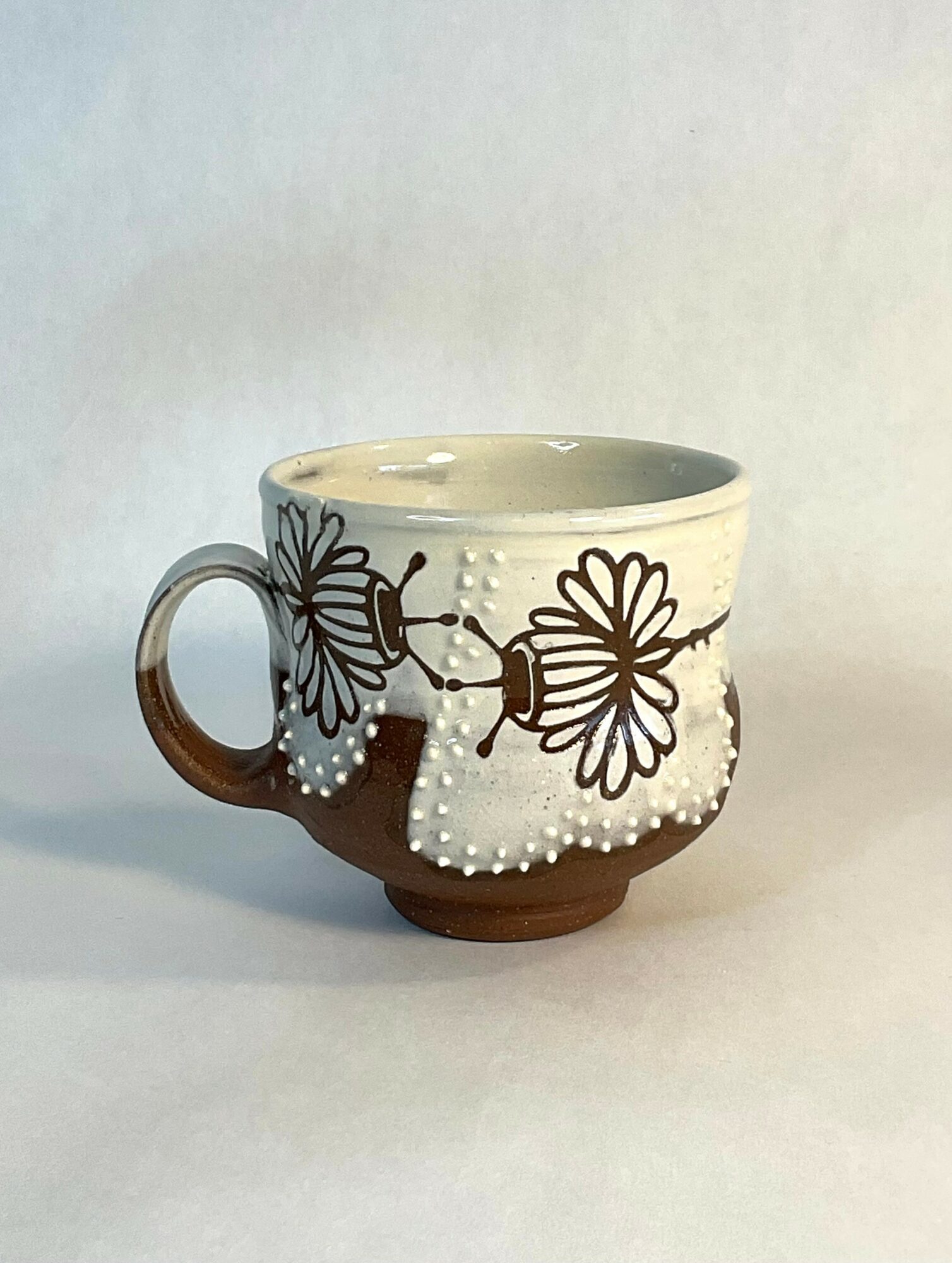 Ceramic mug with floral and butterfly design, partially glazed in brown and cream colors, on a plain background.
