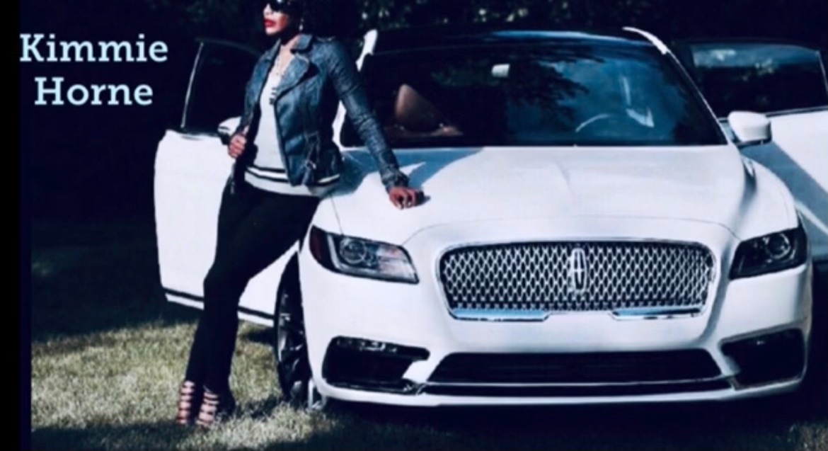 Person standing next to a white luxury car outdoors, with text 'Kimmie Horne' in the top left corner.