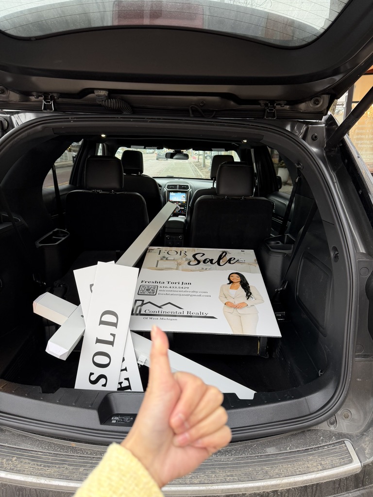 Open car trunk with sale signs and a person's hand giving a thumbs-up inside the vehicle.