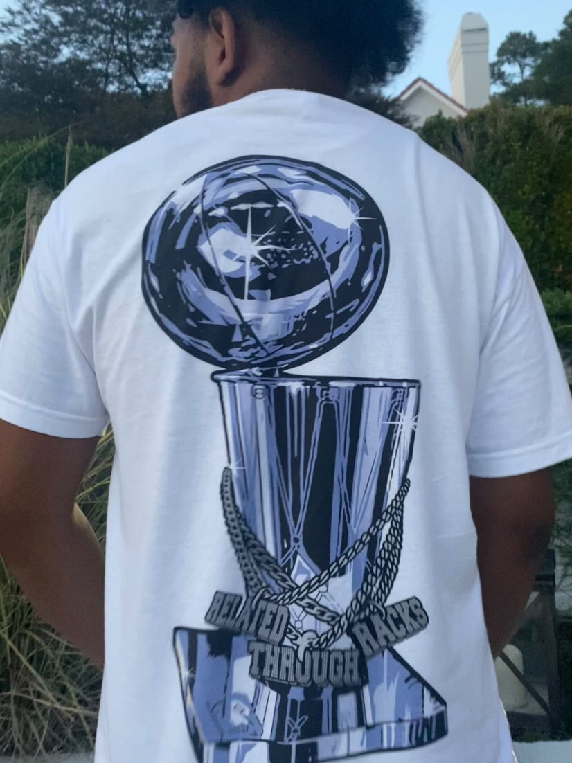 Person wearing a white T-shirt with a large graphic of a trophy and a globe on the back, outdoors.