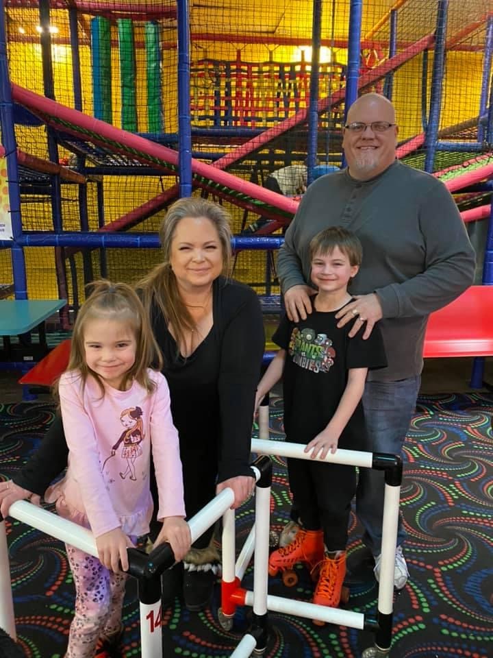 Group of four people, two children and two adults, smiling inside an indoor playground with colorful structures.
