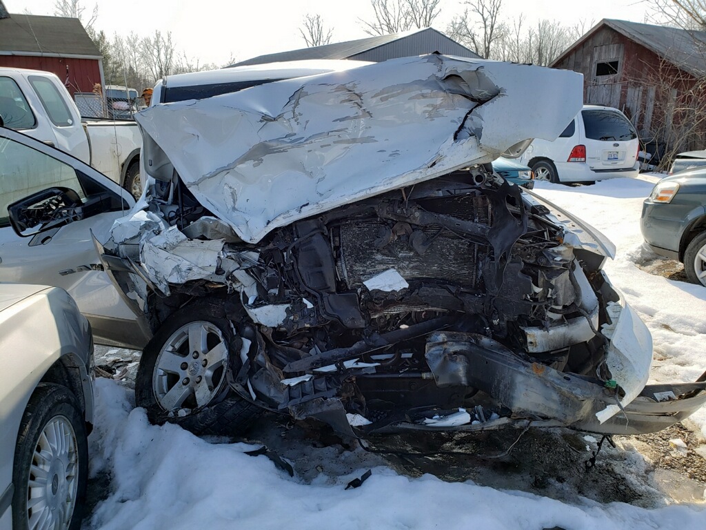 Crushed and damaged vehicle with a large metal piece bent and crumpled, surrounded by other cars in a snowy outdoor setting.
