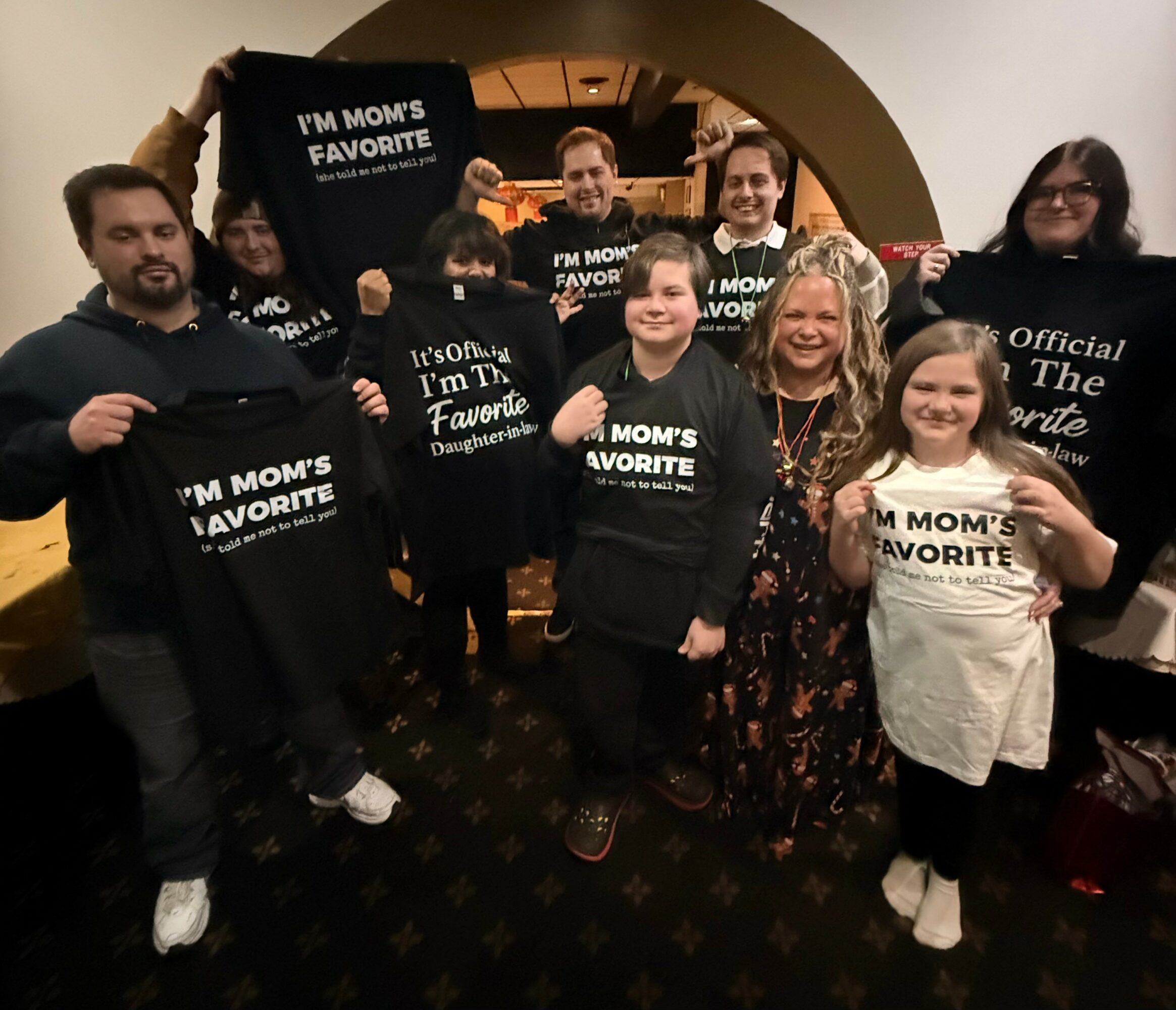 Group of people holding black shirts with white text, standing indoors with a woman in the center, smiling.