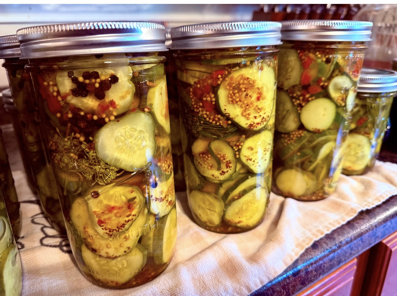 Three glass jars filled with pickled vegetables and spices, sealed with metal lids, on a cloth surface.