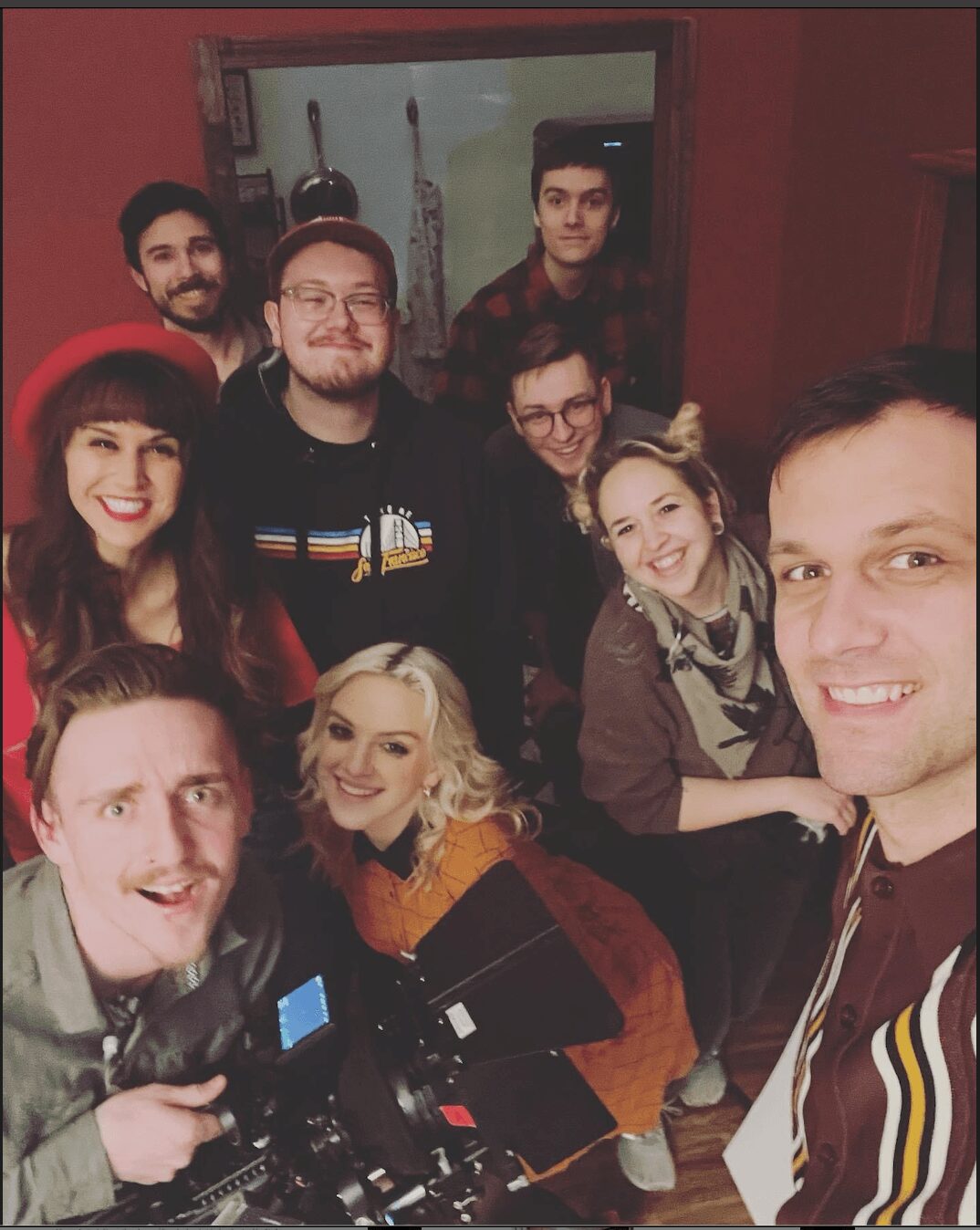 Group of nine people smiling indoors, some wearing hats, gathered around a table with equipment, posing for a photo.