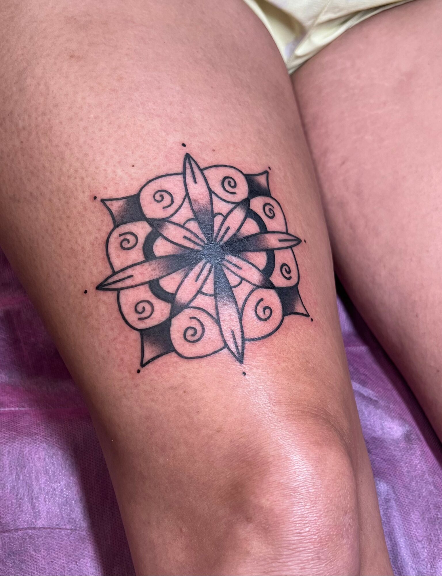 Tattoo of a symmetrical geometric design with swirling patterns and a central star-like shape on skin.