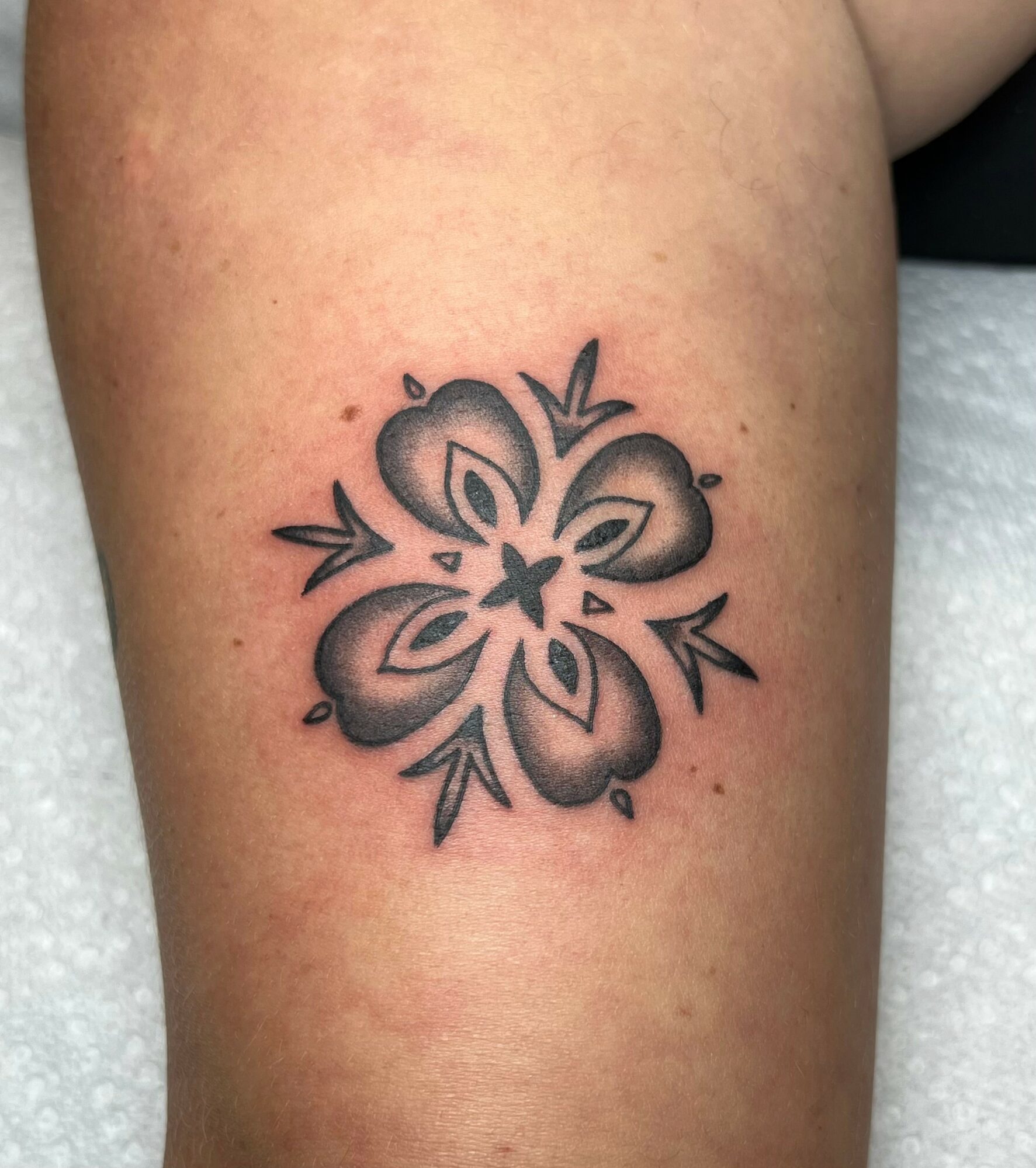 Black and gray flower tattoo with five petals and leaf accents on skin.
