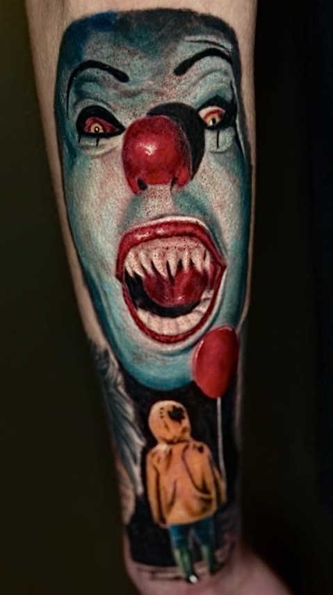 Tattoo of a clown with red nose and sharp teeth, holding a balloon, and a person in a hoodie below.