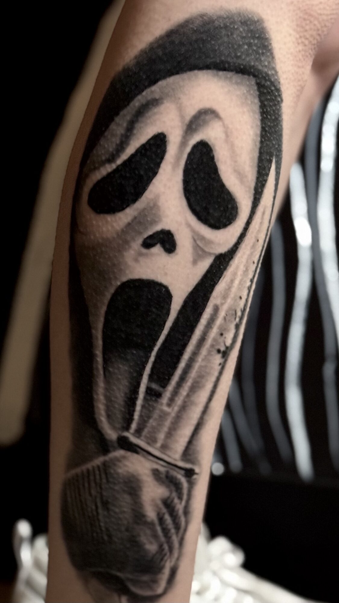Tattoo of a ghost face mask from a horror movie on person's arm, with a knife below it.