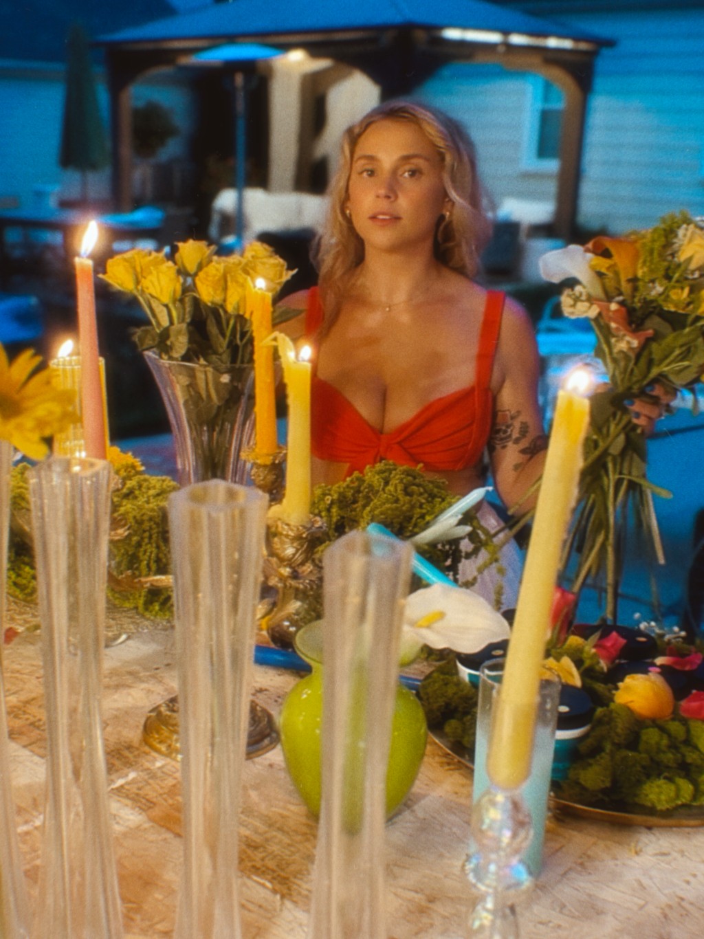Woman in red dress sitting at a table with flowers and candles outdoors at night.